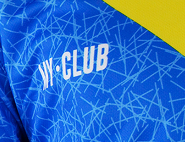 Close-up of a blue fabric with light blue intersecting lines and the word CLUB in white, designed by a kit designer. A yellow diagonal section appears at the top right, perfect inspiration for personalised football kits.