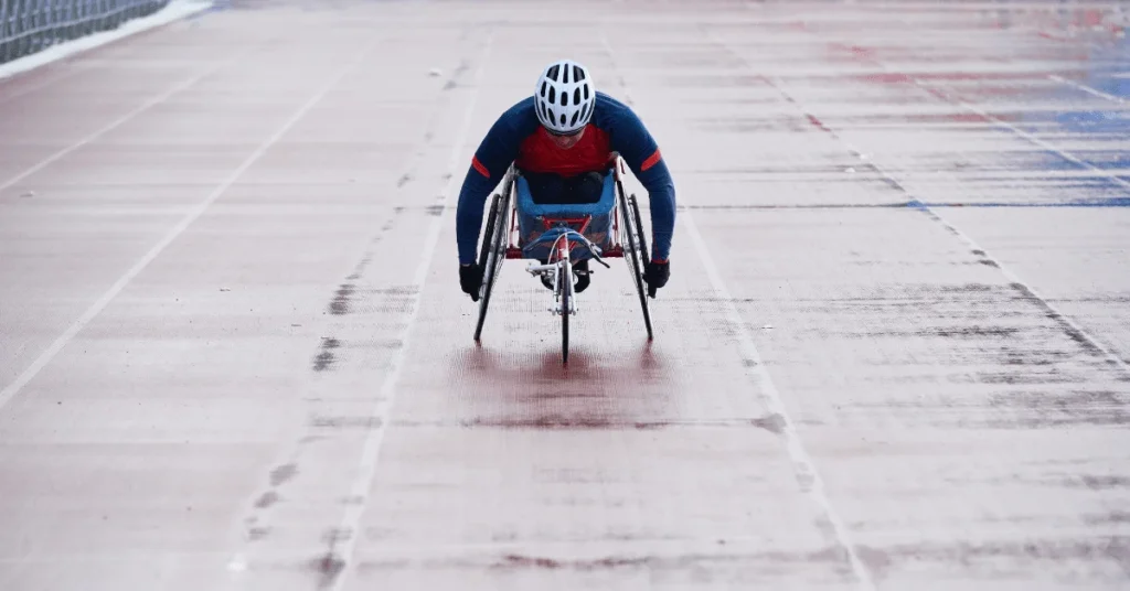 Eine Person, die einen Helm und eine Sportausrüstung trägt, nimmt an einem Rollstuhlrennen auf einer nassen Strecke im Freien teil und drängt entschlossen vorwärts - ähnlich wie Sportler, die bei intensiven Spielen stolz ihre individuellen Fußballtrikots tragen.