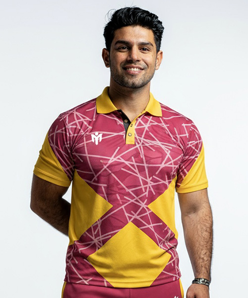 A man with short dark hair smiles while wearing a maroon and yellow cricket jersey featuring abstract white lines and a logo on the left chest, standing against a plain white background—highlighting the appeal of bespoke sports kits.