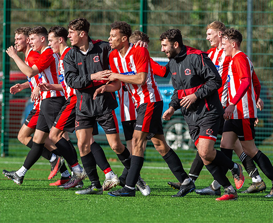 A group of soccer players in red and white uniforms celebrate on a field.