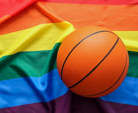 Un balón de baloncesto descansa sobre una bandera del orgullo LGBTQ+ con las rayas del arco iris, símbolo de la inclusión y el apoyo a la diversidad en el deporte, al igual que las equipaciones deportivas a medida que celebran la individualidad dentro y fuera de la cancha.