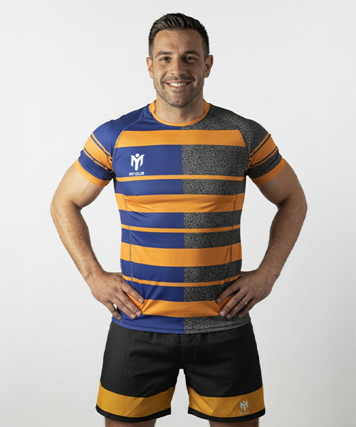 A smiling man stands with hands on hips, wearing a short-sleeved custom football strip featuring orange, blue, and grey horizontal stripes, with matching black shorts. He is posed confidently against a plain white background.