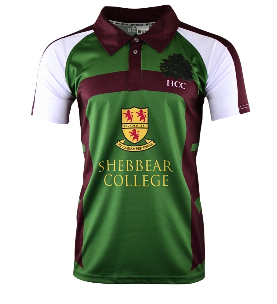 A green, maroon, and white short-sleeved sports jersey with a collar, featuring the HCC logo, a tree graphic, and “SHEBBEAR COLLEGE” printed on the front along with a yellow and red crest.