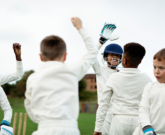 Youth cricket players celebrating on the field in white uniforms and helmets.