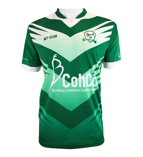 A green and white short-sleeve football shirt with bold geometric patterns, team crest on the left chest, MY-CLUB on the right, and CohCo Building Cohesive Communities logo across the front.