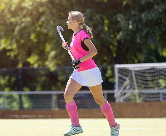 Woman in pink sports attire holding a field hockey stick on a grassy field.