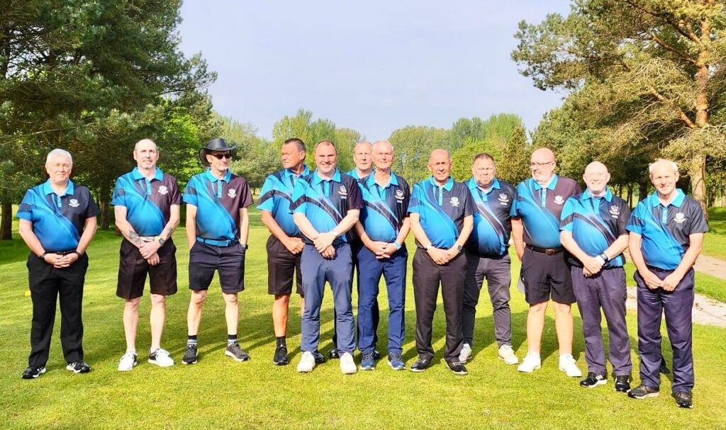 Eine Gruppe von zwölf Männern steht im Freien auf einer Wiese, alle in passenden blau-schwarzen Sporttrikots, mit Bäumen und Sonnenlicht im Hintergrund.