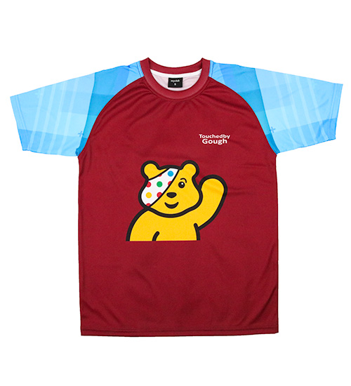 A maroon short-sleeved sports shirt with light blue sleeves featuring an illustration of Pudsey Bear, the Children in Need mascot, and the words Touched by Gough on the chest.