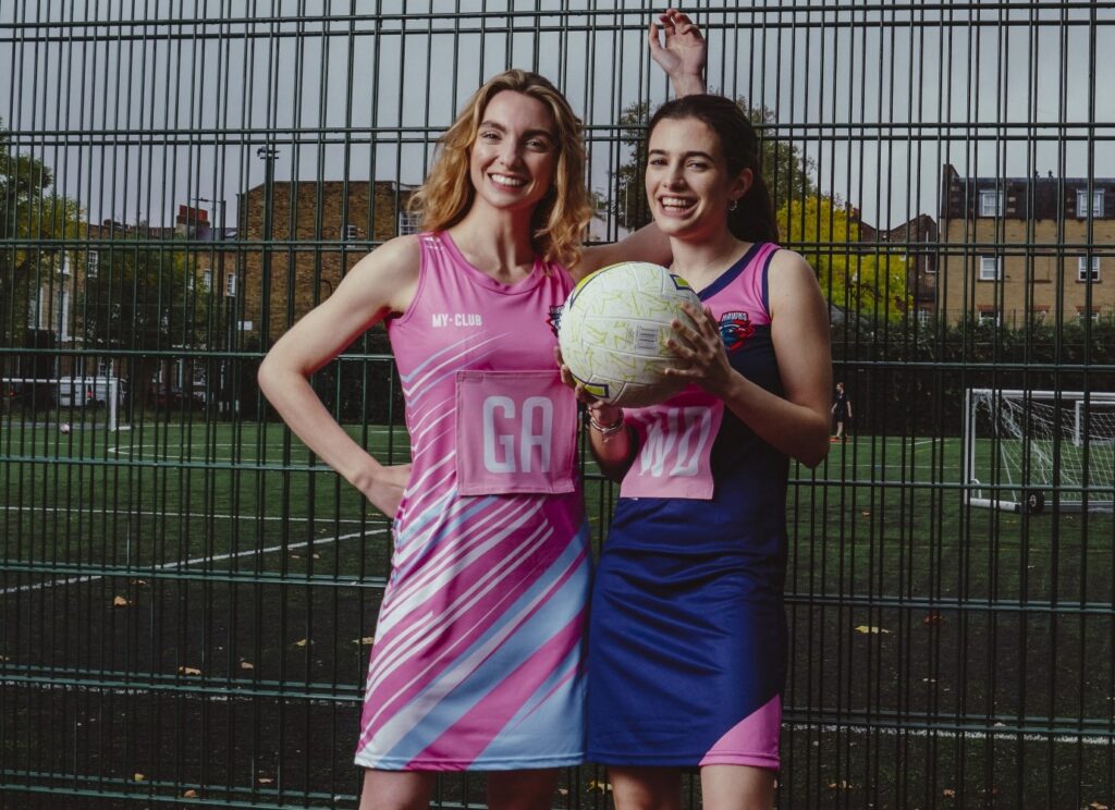Zwei Mädchen lächeln, während sie die maßgeschneiderten Netzballkleider von My Club tragen