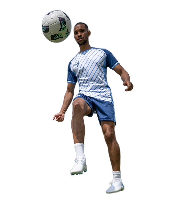 A man in a blue and white football kit juggles a football in mid-air against a plain white background.
