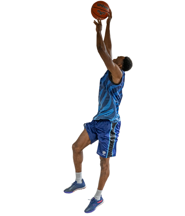 A basketball player in a blue kit jumps with one knee raised, reaching up to shoot a basketball towards the hoop.