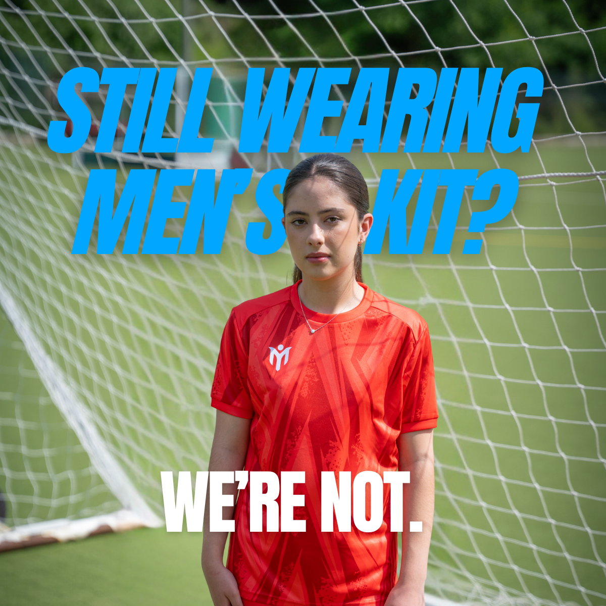 Una joven con una equipación de fútbol roja delante de una portería en un campo de fútbol. Un gran texto en azul dice: ¿Todavía se lleva la equipación de hombre? Texto en blanco debajo: NO.