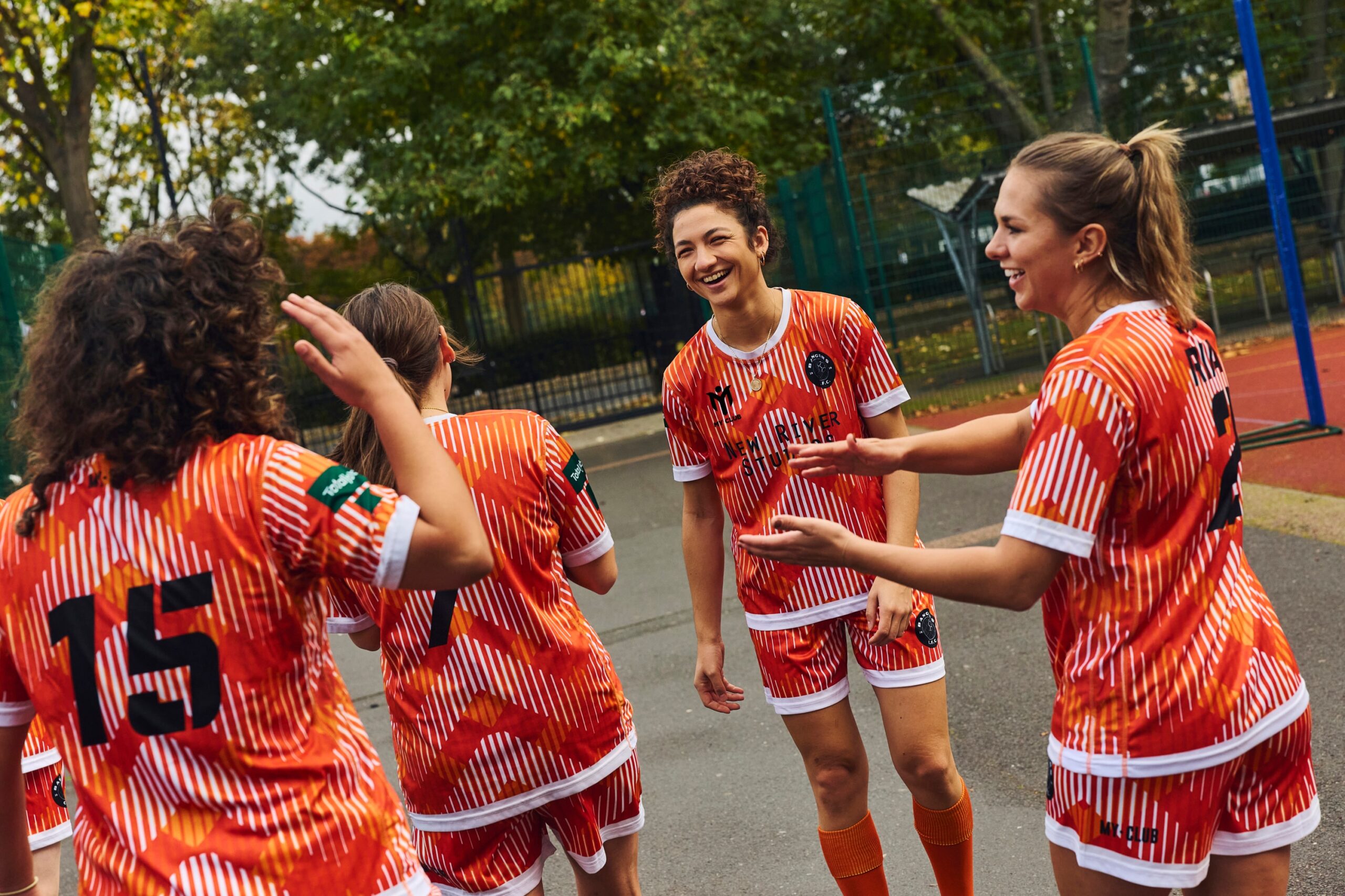 Un grupo de jugadores con uniformes deportivos de colores vivos ríen juntos, mostrando su espíritu de equipo. Las camisetas de fútbol personalizadas presentan diseños únicos, que reflejan sus colores y su escudo.