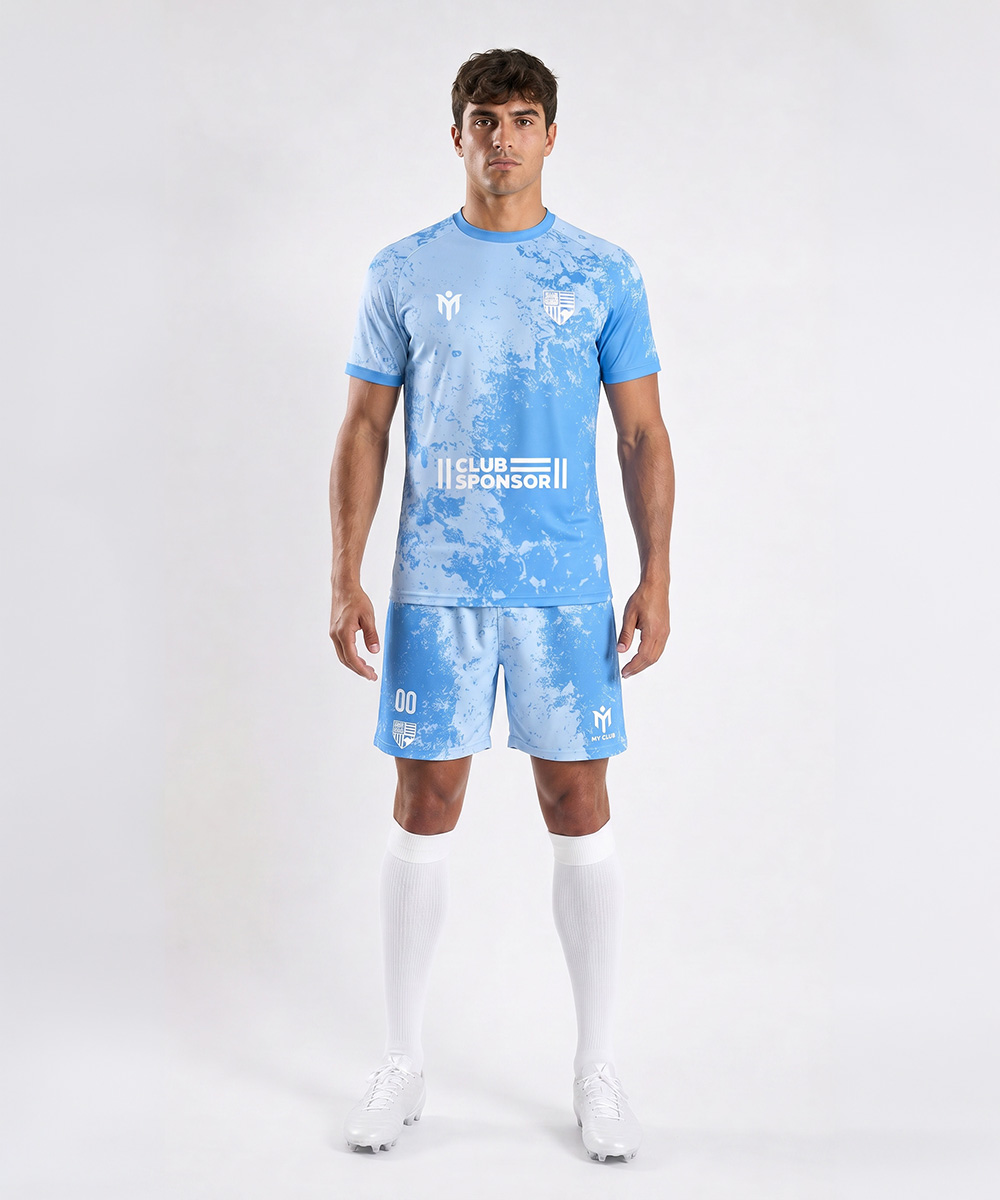 Un uomo è in piedi, rivolto in avanti, e indossa una maglia da calcio su misura azzurra con motivi bianchi, calzettoni bianchi al ginocchio e scarpe da calcio bianche. Sulla maglia è raffigurato un logo, la scritta “Club Sponsor” e il numero 00 sui pantaloncini.
