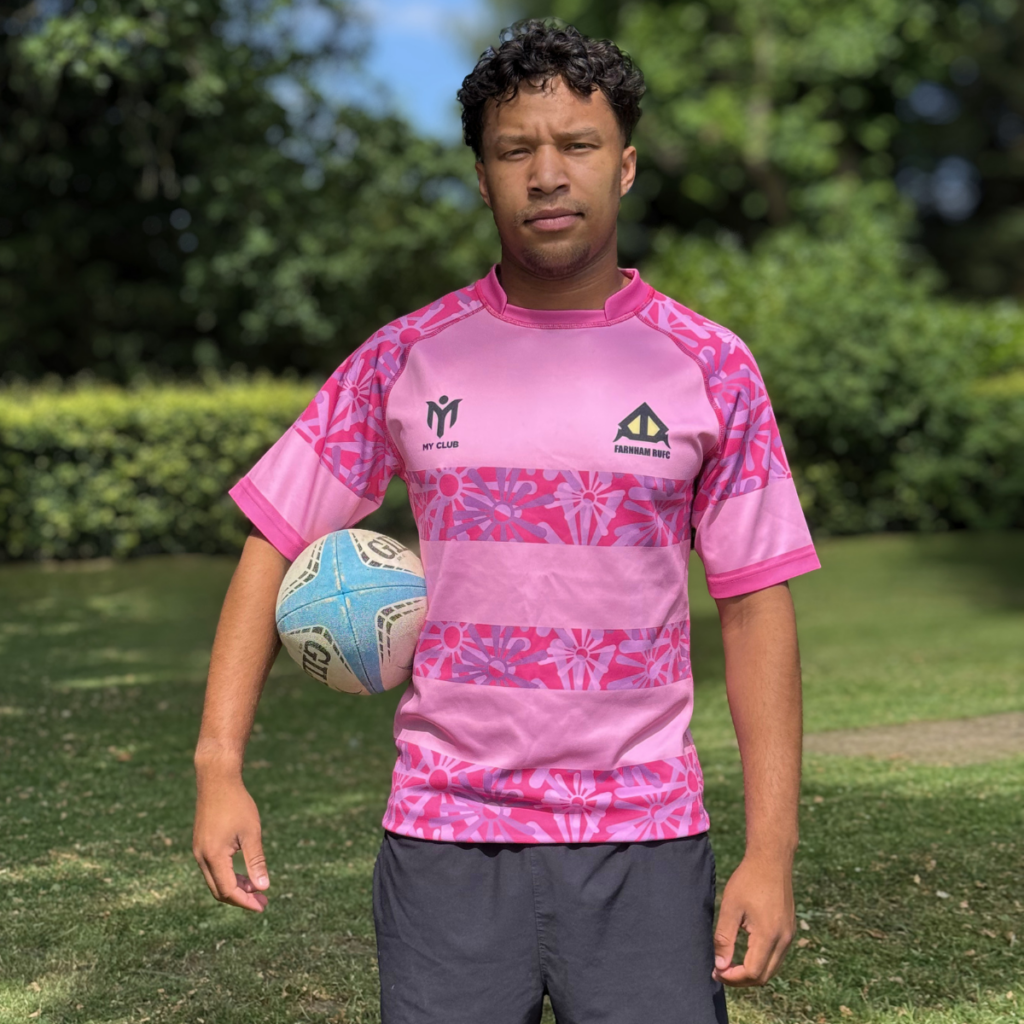 Giocatore di rugby che indossa una maglia personalizzata del Farnham RUFC, stampata a sublimazione in rosa, con il marchio My Club Group, mentre tiene in mano un pallone da rugby