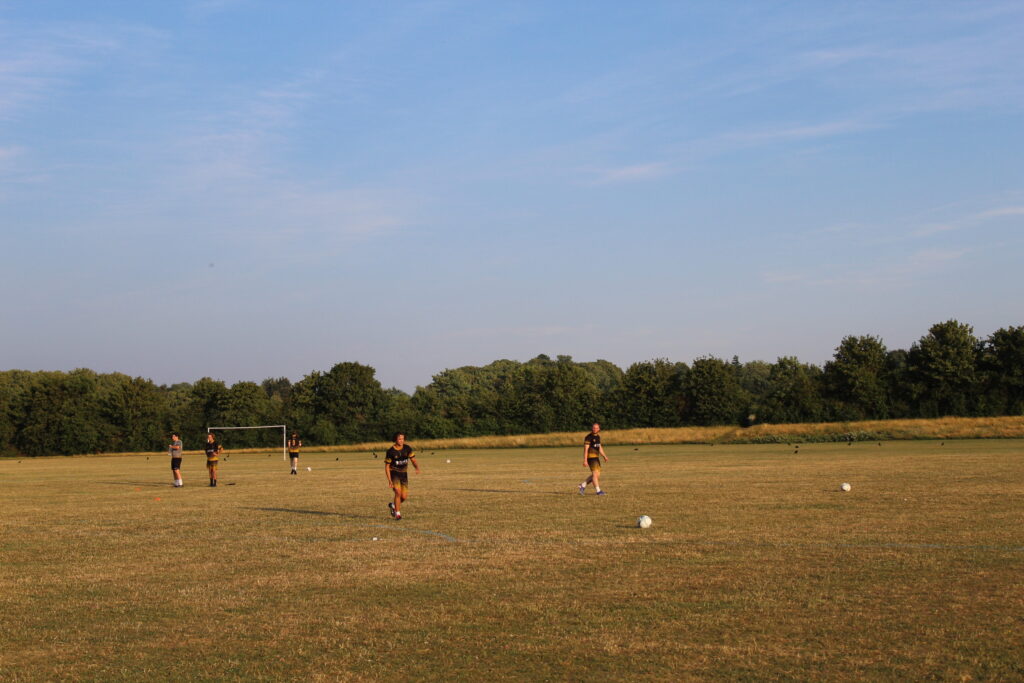 Los jugadores del Golden Warriors FC entrenan con la equipación a juego, en negro y dorado, en un campo de césped durante una sesión vespertina de verano.