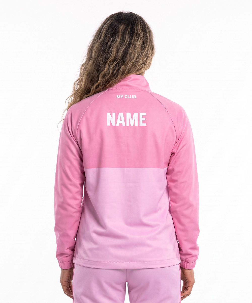 Eine Person mit langen, gewellten Haaren trägt eine rosa Trainingsjacke und eine Trainingshose, von hinten gesehen. Auf dem Rücken der individuell gestalteten Softshell-Jacke ist in weißer Schrift „MY CLUB“ über „NAME“ aufgedruckt. Der Hintergrund ist einfarbig weiß.