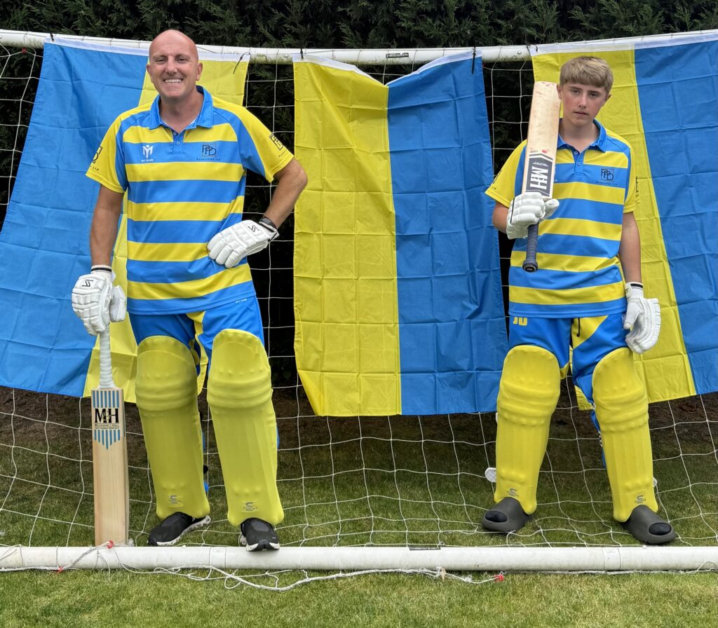 Zwei Spieler des Fylde Cricket Club in blau-gelb gefärbten Trikots, die Schlagpolster und Handschuhe tragen und Cricketschläger in den Händen halten