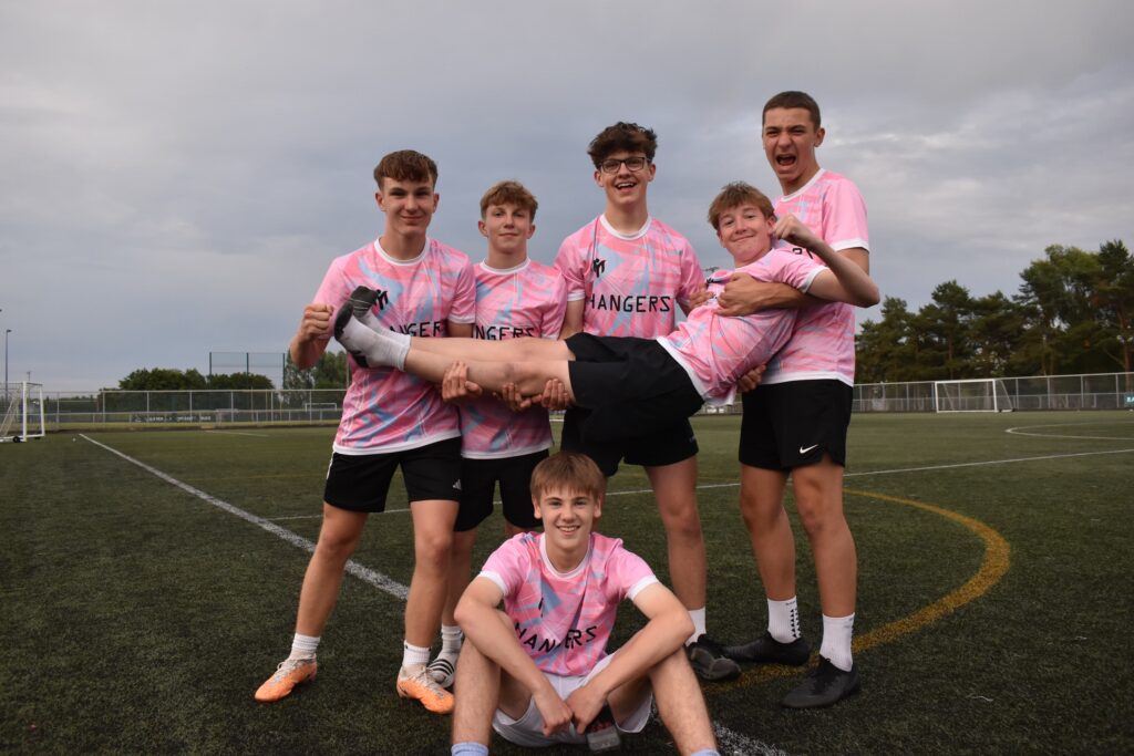 A youth football squad celebrating on the pitch in matching custom pink kits with their club name and black shorts
