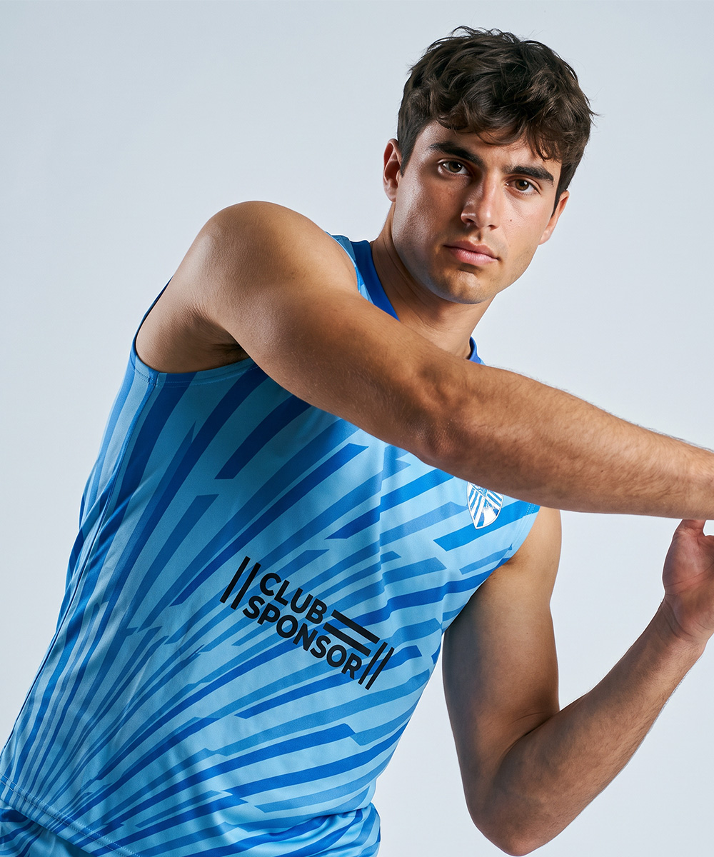 Ein Mann in einem blauen, maßgeschneiderten, ärmellosen Sport-T-Shirt mit der Aufschrift „Club Sponsor“ posiert mit ausgestreckten Armen und blickt direkt in die Kamera vor einem schlichten, hellen Hintergrund.