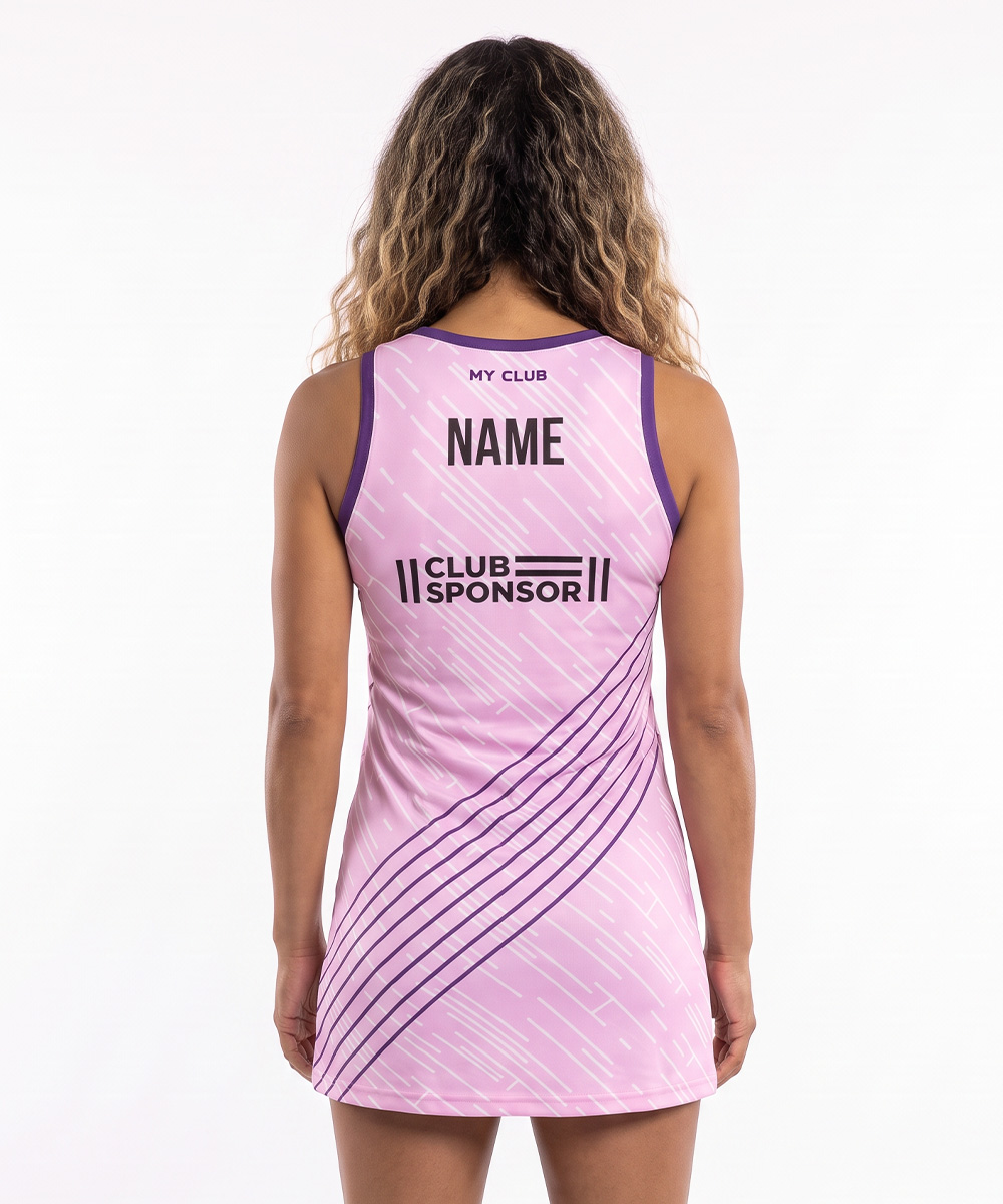 Una persona con lunghi capelli mossi, vista di spalle, indossa una divisa da netball Custom Elite di colore rosa e viola con le scritte MY CLUB, NOME e SPONSOR DEL CLUB sul retro, caratterizzata da eleganti strisce diagonali.