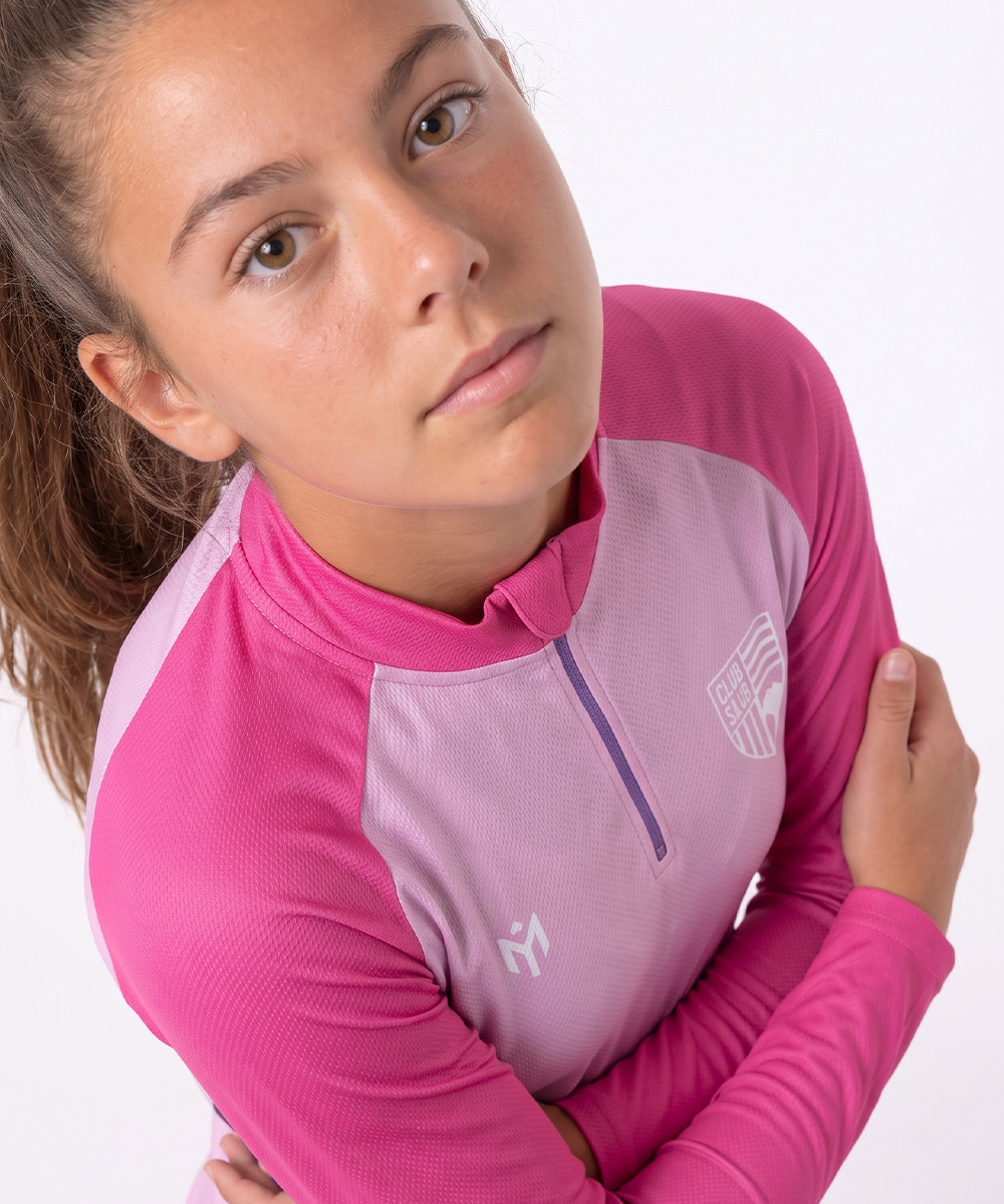 Ein junges Mädchen, das ein maßgeschneidertes, langärmeliges Radtrikot in Rosa und Hellviolett mit einem Logo auf der Brust trägt.