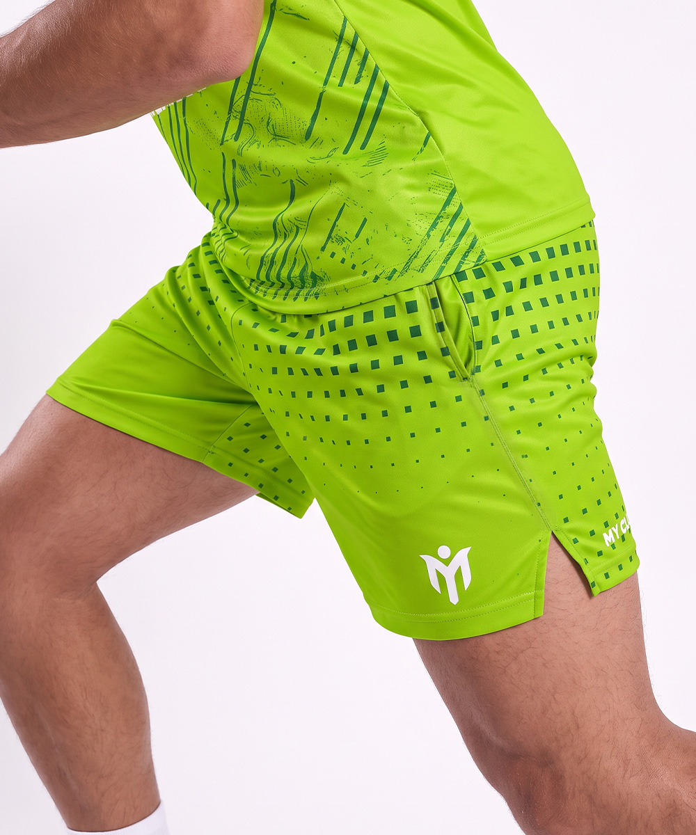 Une personne portant un maillot de sport vert citron et un short de tennis personnalisé, fabriqué à partir de matériaux recyclés, orné d'un motif carré et d'un logo blanc sur la jambe.