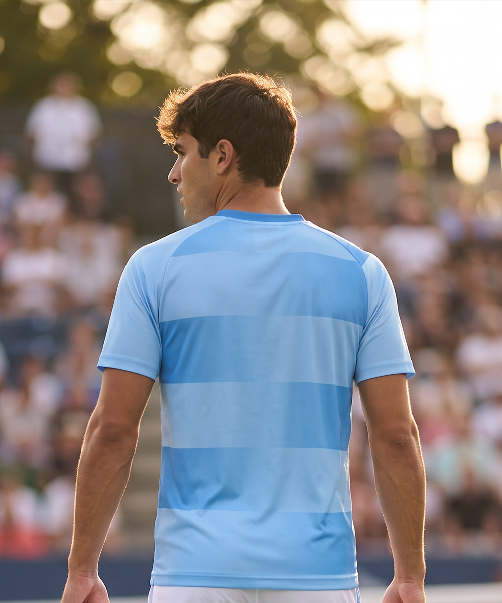 Un homme vu de dos, vêtu d'un polo de tennis sur mesure à rayures horizontales bleu clair, dans un stade bondé.